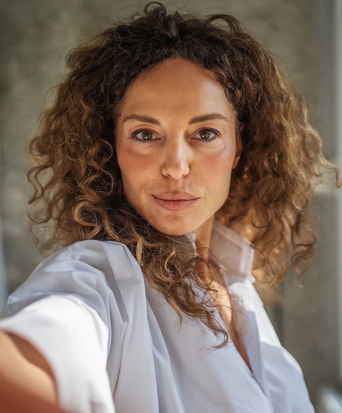 Smiling woman with curly hair taking selfie.